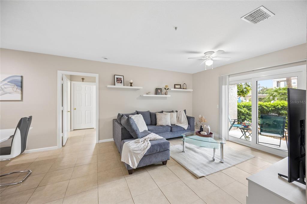 A living room features a blue sectional sofa, floating shelves, tile flooring, and sliding glass doors — 6596 SWISSCO DRIVE UNIT 1512, ORLANDO, FL