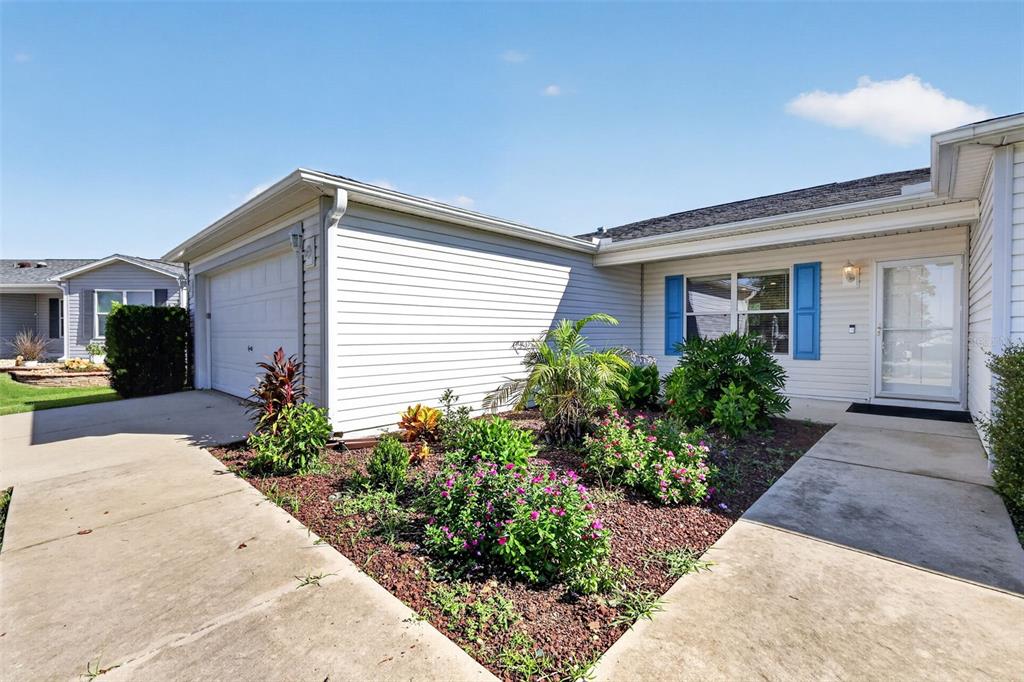 A single-story house exterior features light siding, a garage, and a front garden bed — 2112 KERWOOD LOOP, THE VILLAGES, FL