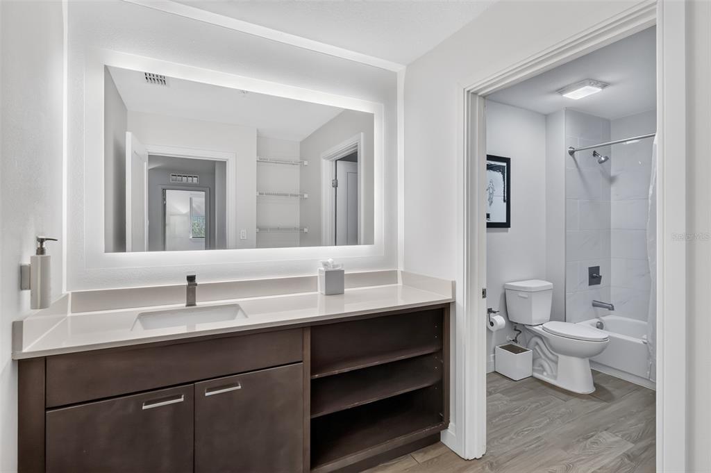 A modern bathroom features a dark wood vanity, a backlit mirror, and an adjoining toilet area — 14501 GROVE RESORT AVENUE UNIT 3438, WINTER GARDEN, FL