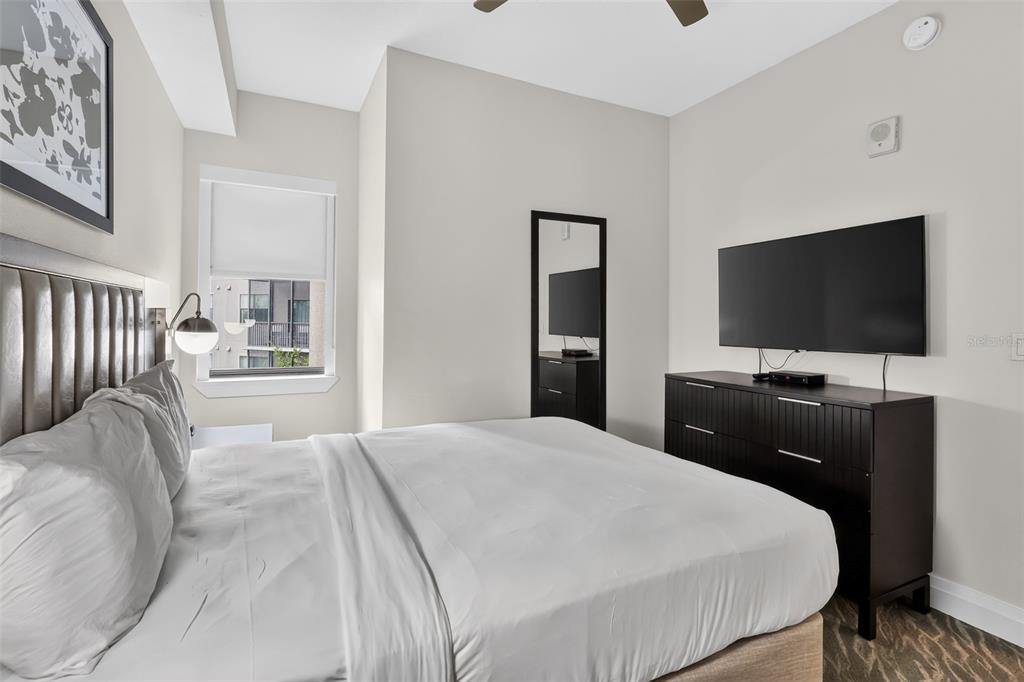 A bedroom features a bed with a tufted headboard, a dresser with a television, and a window — 14501 GROVE RESORT AVENUE UNIT 3438, WINTER GARDEN, FL