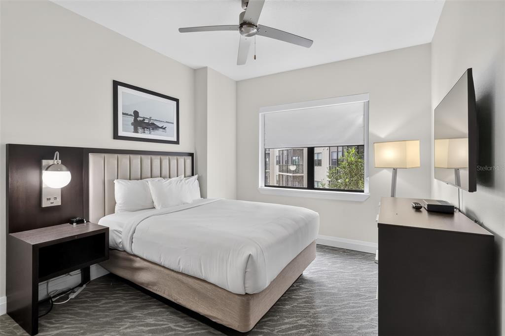 A bedroom features a queen bed, a dark wood nightstand, a television, and a ceiling fan — 14501 GROVE RESORT AVENUE UNIT 3438, WINTER GARDEN, FL