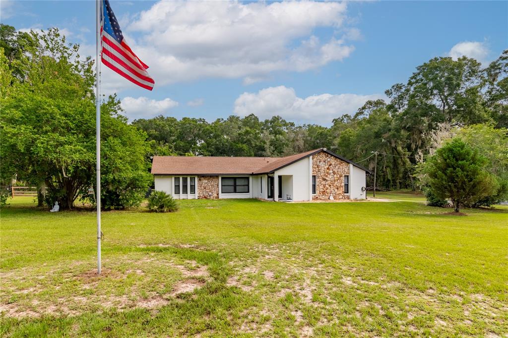 A single-story house with stone accents and a large lawn under a sunset sky — 2735 NE 127TH PLACE, ANTHONY, FL