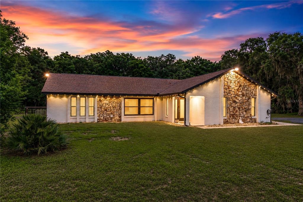 A backyard view of a house with a wooden pergola, string lights, and sunset sky — 2735 NE 127TH PLACE, ANTHONY, FL