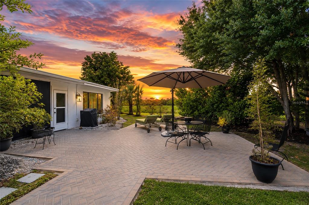 A paved patio with outdoor furniture and an umbrella overlooks a sunset landscape — 3602 JOYCE DRIVE, BRADENTON, FL
