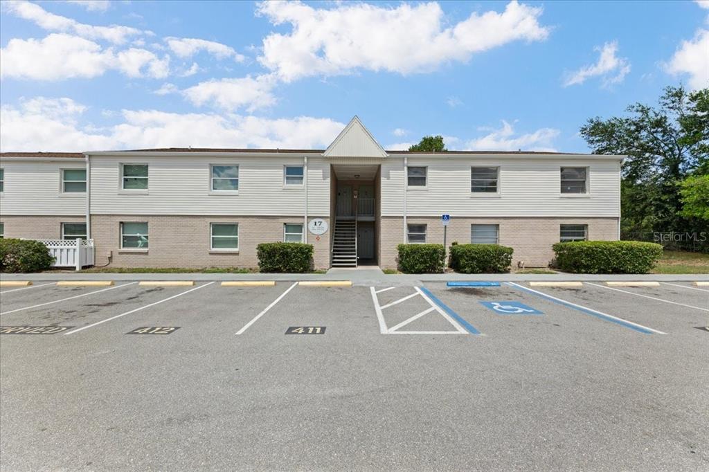 A two-story apartment building with beige brick and white siding stands behind a parking lot — 7210 N MANHATTAN AVENUE UNIT 1714, TAMPA, FL