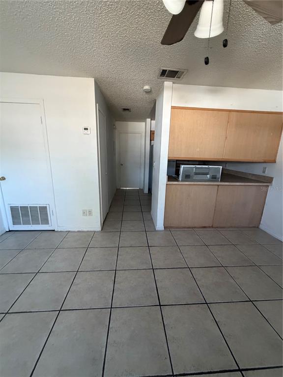 A room with light-colored tile flooring, a ceiling fan, and wooden kitchen cabinets — 1 LAKE VILLA WAY, KISSIMMEE, FL