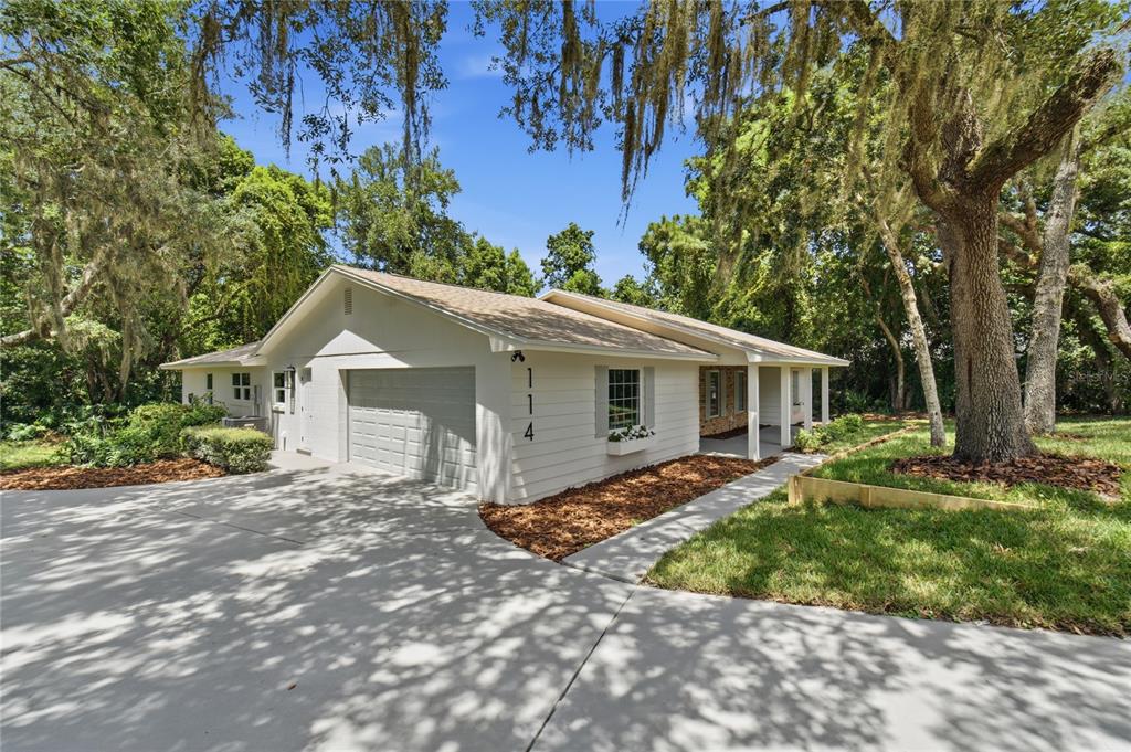 A single-story house with white siding, a garage, and a covered porch under large trees — 114 WAYLAND CIRCLE, LONGWOOD, FL