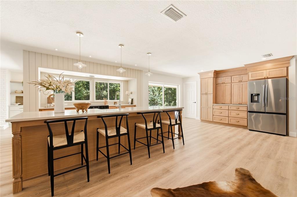A kitchen features a large island with bar stools, light wood cabinets, and stainless appliances — 114 WAYLAND CIRCLE, LONGWOOD, FL