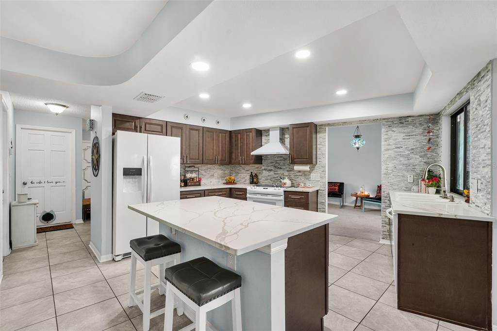 A kitchen with dark wood cabinets, white quartz countertops, a central island, and tile flooring — 2715 BERRYKNOLL PLACE, VALRICO, FL