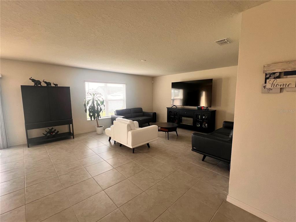 A living room features tile flooring, a white armchair, two black sofas, and a television console — 3209 EAGLE HAMMOCK CIRCLE, KISSIMMEE, FL