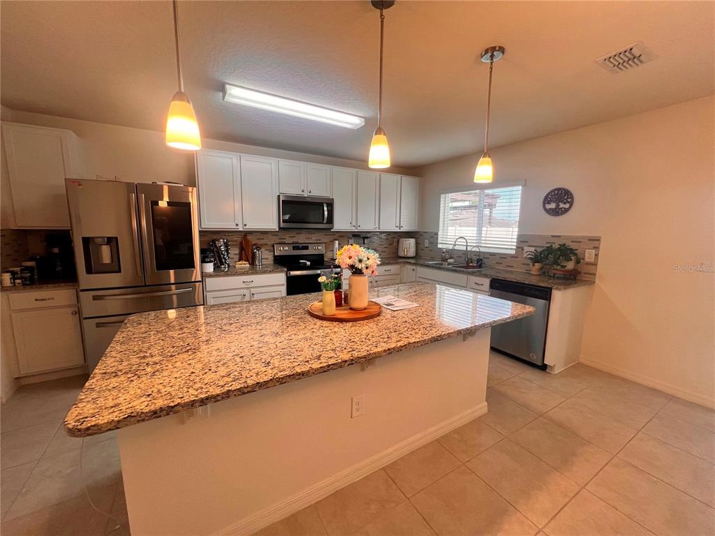 A kitchen features white cabinets, granite countertops, a large island, and stainless steel appliances — 3209 EAGLE HAMMOCK CIRCLE, KISSIMMEE, FL