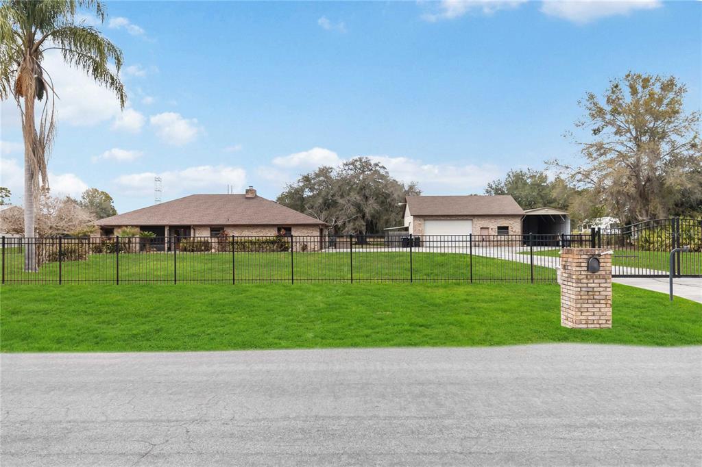 A grassy yard leads to a brick house and a detached garage under a blue sky — 18711 NORTHCLIFF STREET, ORLANDO, FL