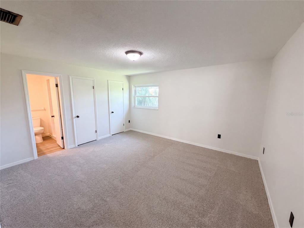 An empty bedroom features white walls, beige carpeting, two closet doors, and an attached bathroom — 1148 WENTWORTH CIRCLE, ROCKLEDGE, FL