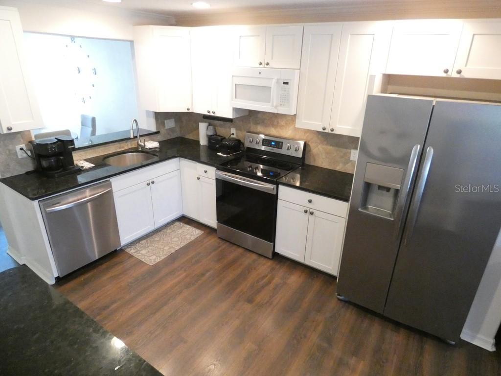 A kitchen with white cabinets, stainless steel appliances, and dark countertops on wood-look flooring — 2554 SEA WIND WAY, CLEARWATER, FL