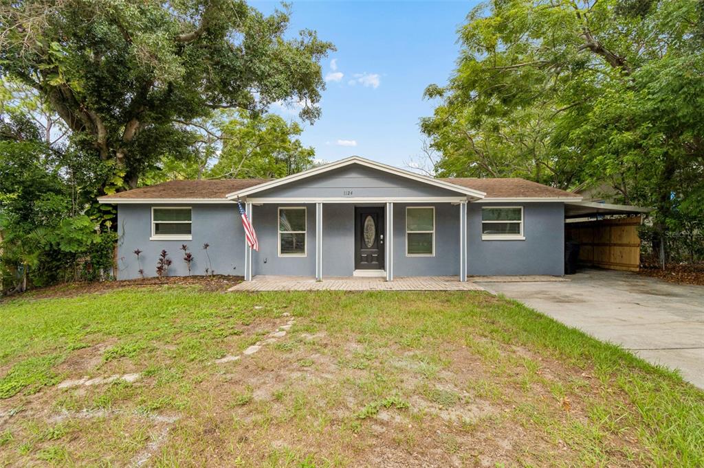 A single-story gray house with a front porch, a concrete driveway, and mature trees — 1124 JADEWOOD AVENUE, CLEARWATER, FL