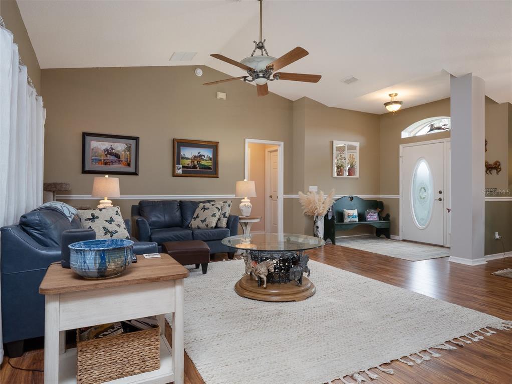 A living room features blue leather sofas, a glass-topped coffee table, and a white front door — 9481 W HIGHWAY 316, REDDICK, FL