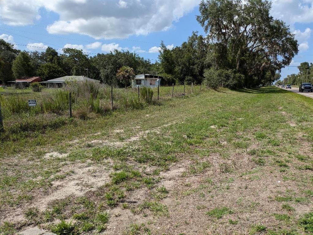A grassy, vacant lot sits beside a road with a fence and houses in the background — 17201 US HIGHWAY 41, SPRING HILL, FL
