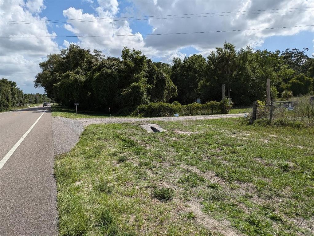 A paved road runs alongside a grassy lot with a gravel driveway and dense trees — 17201 US HIGHWAY 41, SPRING HILL, FL