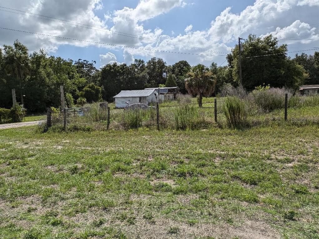A grassy, fenced lot features a small, weathered white structure and surrounding trees — 17201 US HIGHWAY 41, SPRING HILL, FL