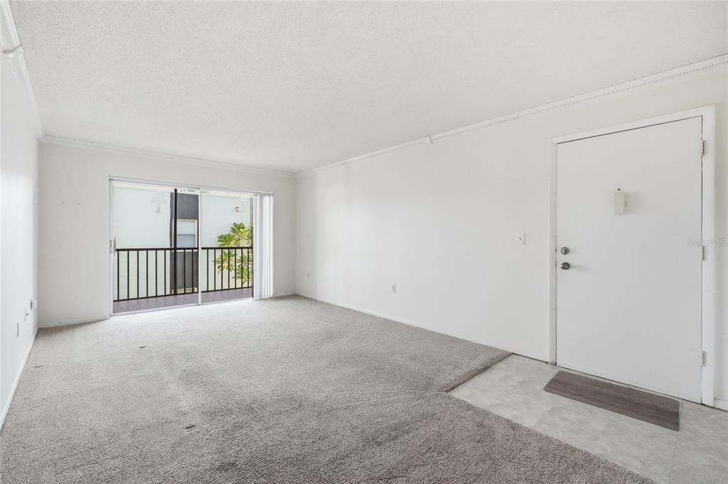 An empty living room with gray carpet, white walls, a sliding glass door, and an entryway — 3267 BENEVA ROAD UNIT 203, SARASOTA, FL