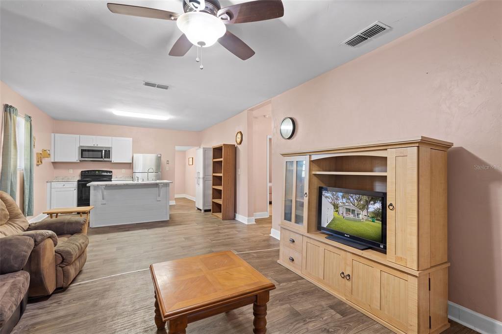 A living room with wood-look flooring opens to a kitchen with white cabinets and appliances — 729 NW 3RD AVENUE, TRENTON, FL