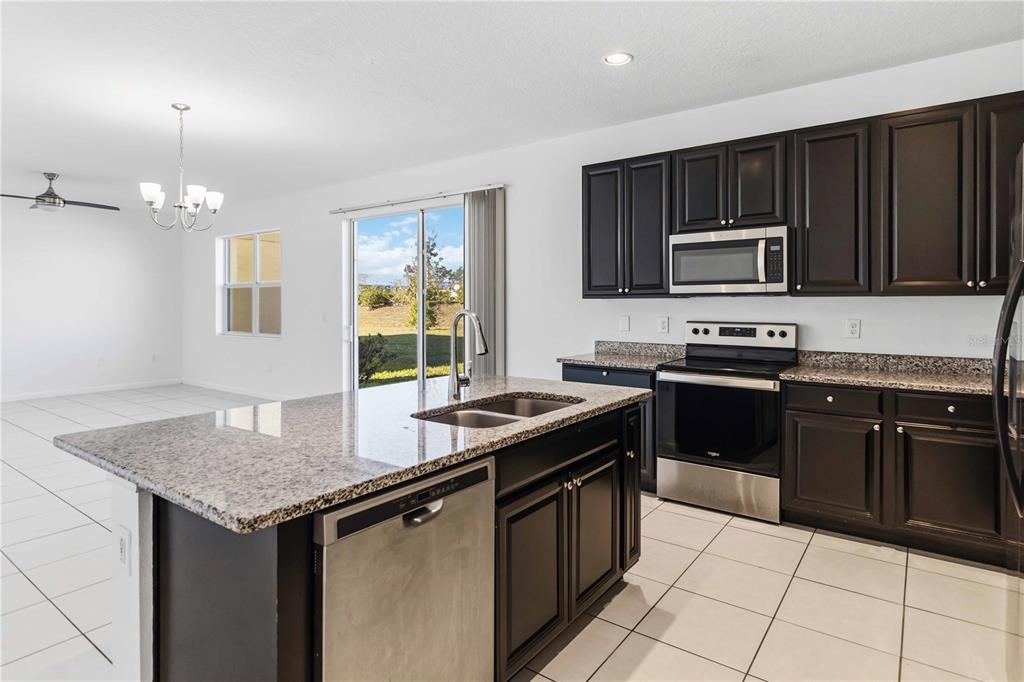 A kitchen features dark cabinets, granite countertops, a central island with bar seating, and stainless appliances — 213 TRINITY RIDGE CIRCLE, DAVENPORT, FL