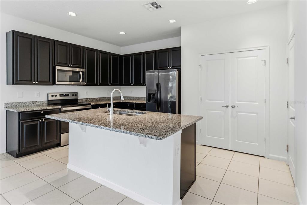 A kitchen features dark cabinets, granite countertops, a stainless steel refrigerator, and a center island — 213 TRINITY RIDGE CIRCLE, DAVENPORT, FL