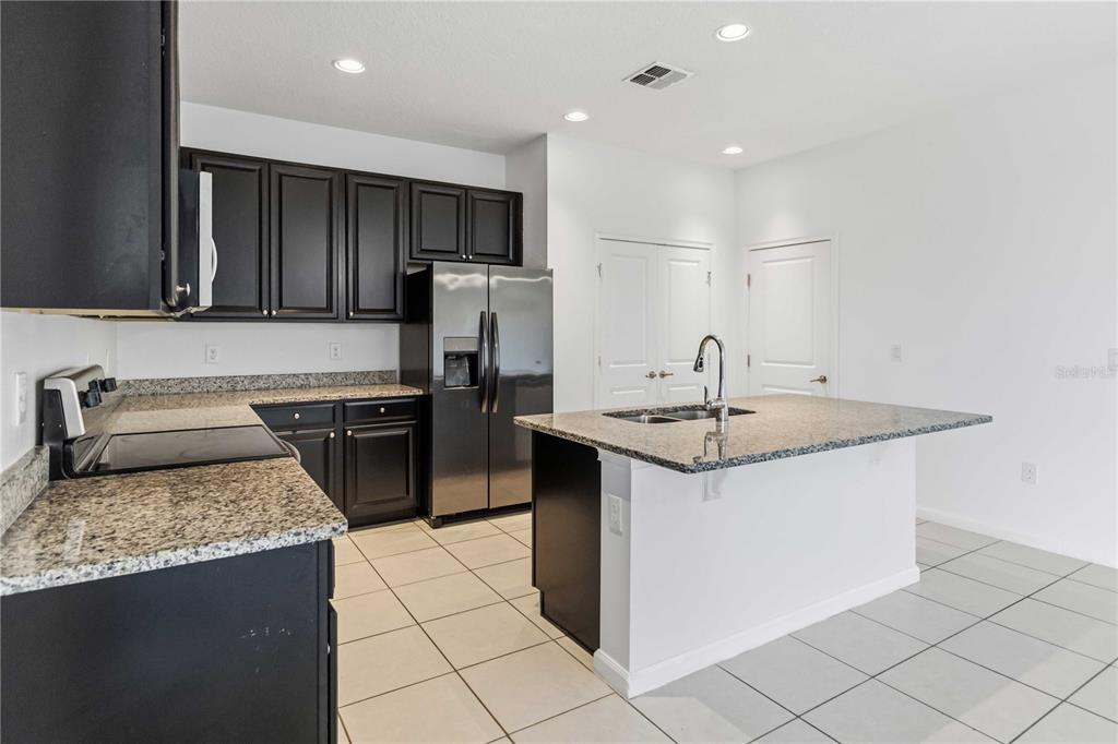 A kitchen island with a granite countertop and sink overlooks a dining area — 213 TRINITY RIDGE CIRCLE, DAVENPORT, FL