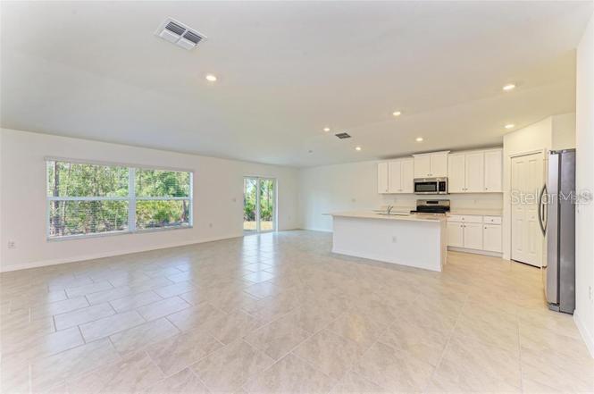 An open-concept kitchen and living area features light tile flooring, white cabinetry, and large windows — 1485 PULASKI STREET, PORT CHARLOTTE, FL
