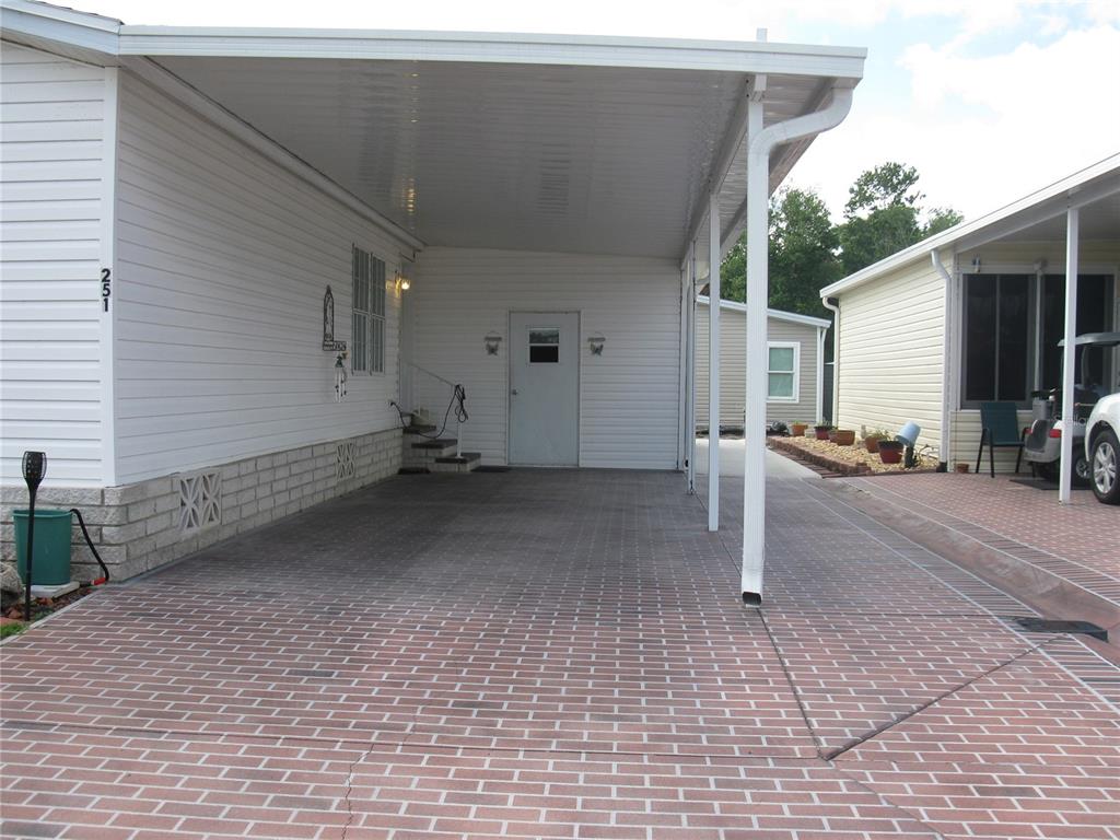 A white mobile home features a covered carport with a red brick-patterned concrete driveway — 251 RAMSGATE WAY, HAINES CITY, FL