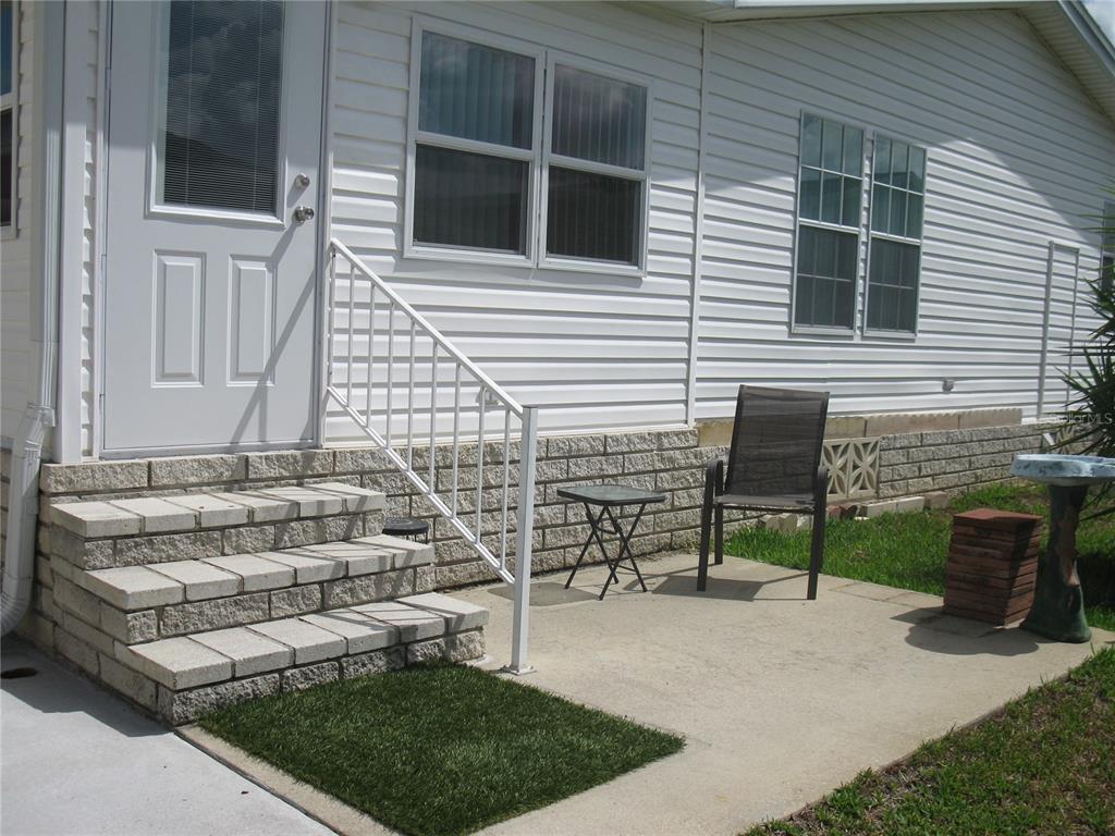 A white mobile home exterior features concrete steps, a small patio, and a metal railing — 251 RAMSGATE WAY, HAINES CITY, FL