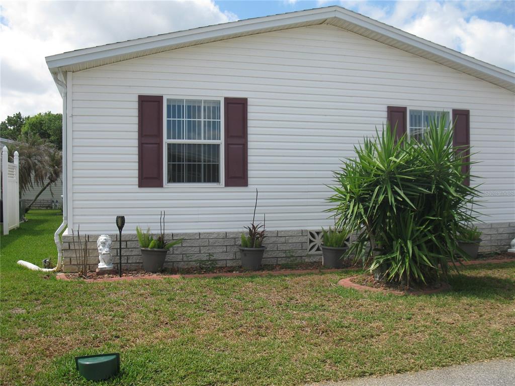 The exterior of a white mobile home features maroon shutters and a landscaped front yard — 251 RAMSGATE WAY, HAINES CITY, FL