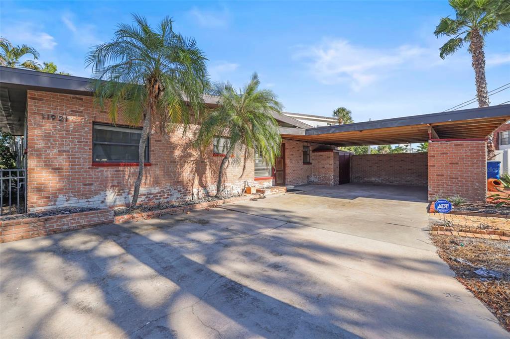 A single-story brick house with a flat roof, palm trees, and an attached carport — 11921 LAGOON LANE, TREASURE ISLAND, FL