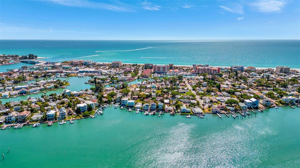 An aerial view shows a coastal neighborhood with houses along a canal and the ocean — 13121 4TH STREET E UNIT 1, MADEIRA BEACH, FL