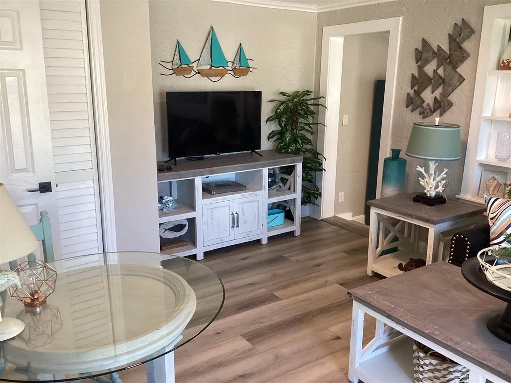 A living room features a television on a white console, wood-look flooring, and coastal decor — 13121 4TH STREET E UNIT 1, MADEIRA BEACH, FL