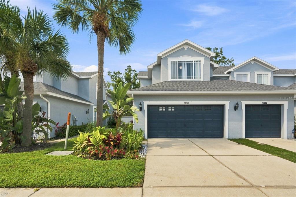 A two-story townhouse with light blue siding, dark garage doors, and a palm tree — 6030 PARKSIDE MEADOW DRIVE, TAMPA, FL
