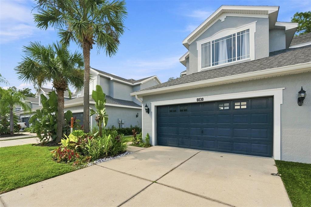 A two-story house with a blue garage door, gray siding, and a palm tree in front — 6030 PARKSIDE MEADOW DRIVE, TAMPA, FL