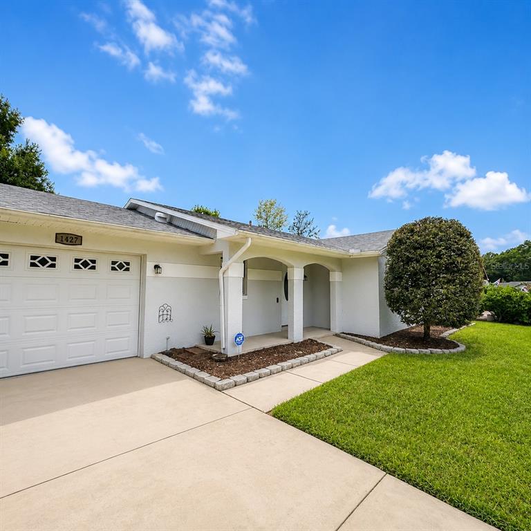 A single-story house exterior features a white garage, a covered entryway, and a landscaped lawn — 1427 BENWICK WAY, CASSELBERRY, FL