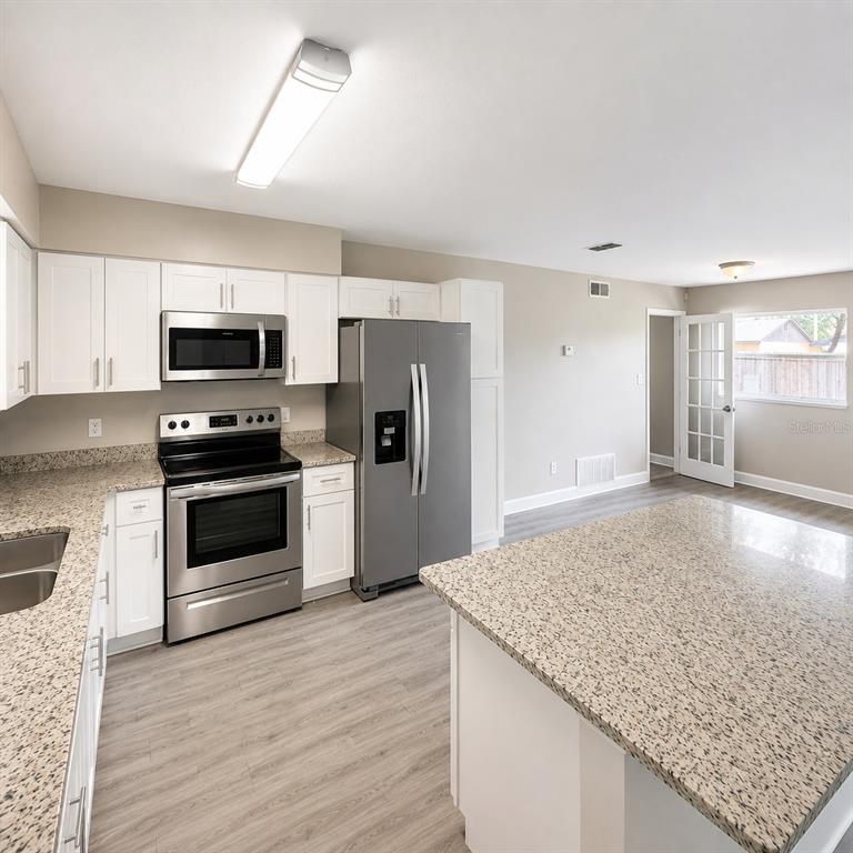 A kitchen features white cabinets, granite countertops, stainless steel appliances, and light wood-look flooring — 1427 BENWICK WAY, CASSELBERRY, FL