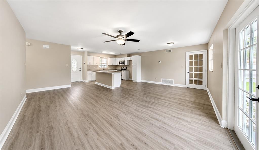 An open-concept living area features light wood-look flooring, a kitchen island, and a ceiling fan — 1427 BENWICK WAY, CASSELBERRY, FL