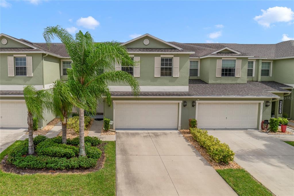A two-story townhouse exterior features green stucco walls, two garage doors, and a palm tree — 3349 RODRICK CIRCLE, ORLANDO, FL