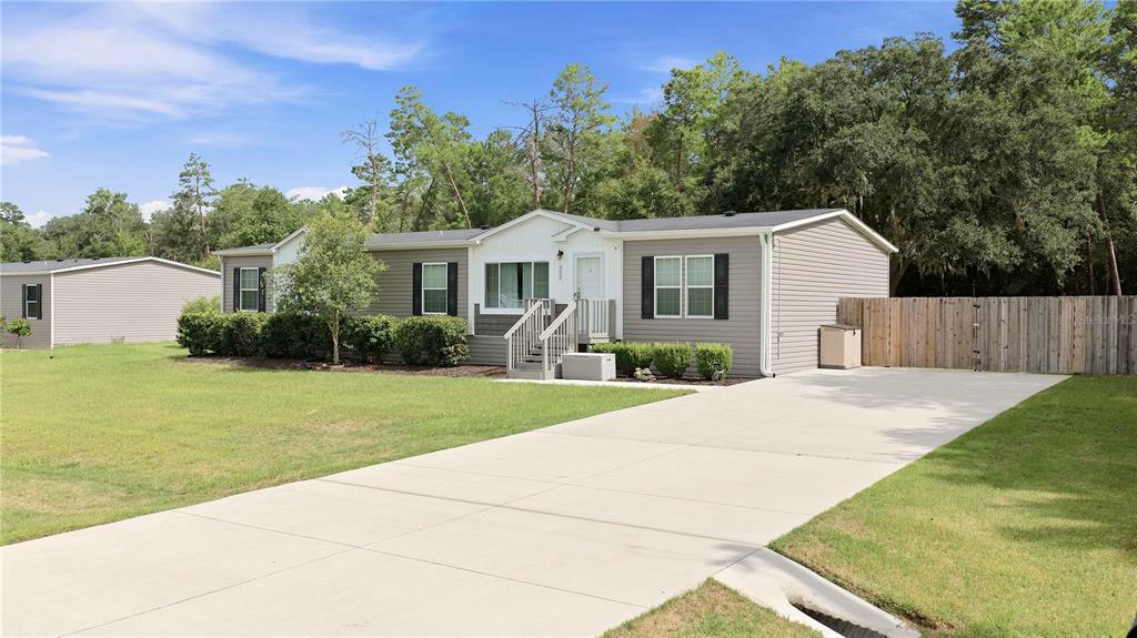 A single-story manufactured home with grey siding, a concrete driveway, and a wooden privacy fence — 122 SE 70TH CIRCLE, OCALA, FL