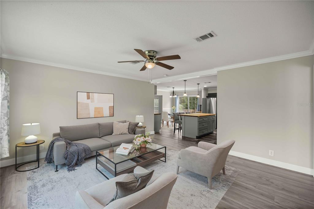 A living room with gray flooring, a sofa, two armchairs, and an open kitchen view — 122 SE 70TH CIRCLE, OCALA, FL