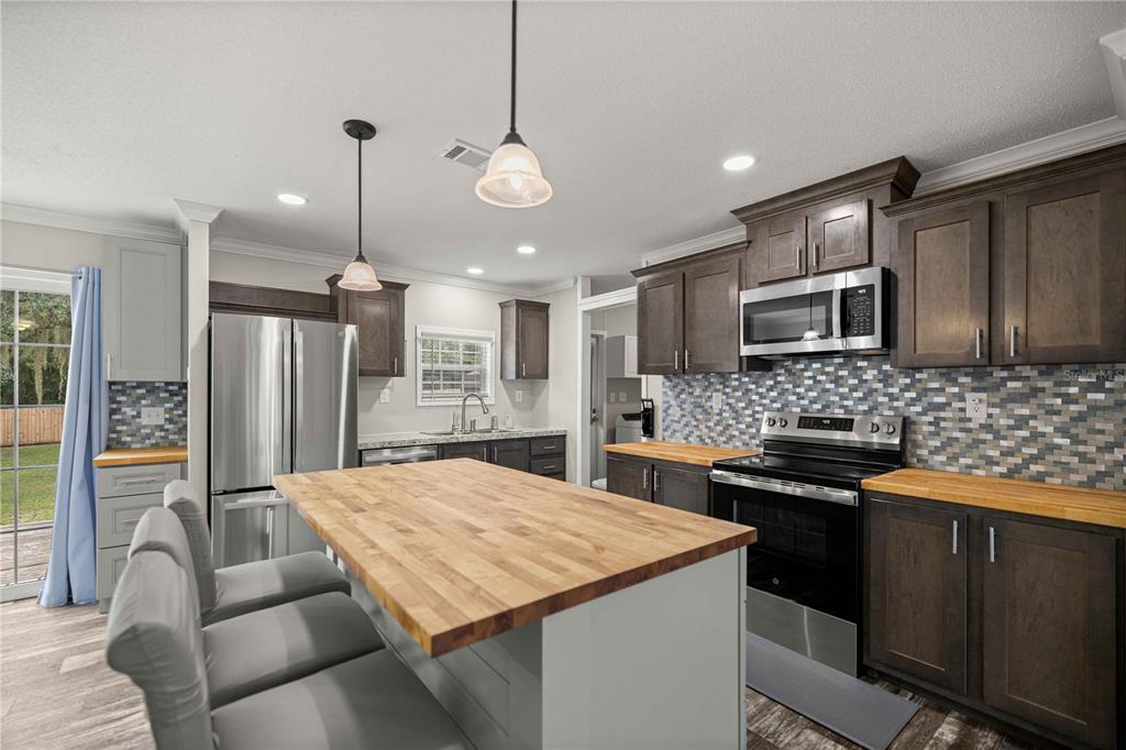 A kitchen features a wooden island, dark cabinetry, stainless steel appliances, and a tiled backsplash — 122 SE 70TH CIRCLE, OCALA, FL