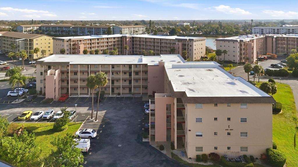 An aerial view shows a multi-story apartment complex with a parking lot and palm trees — 4143 HERON WAY 207 BLDG E, BRADENTON, FL