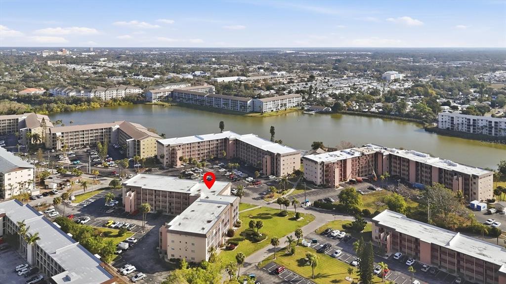 An aerial view shows multiple multi-story apartment buildings surrounding a lake with parking lots — 4143 HERON WAY 207 BLDG E, BRADENTON, FL