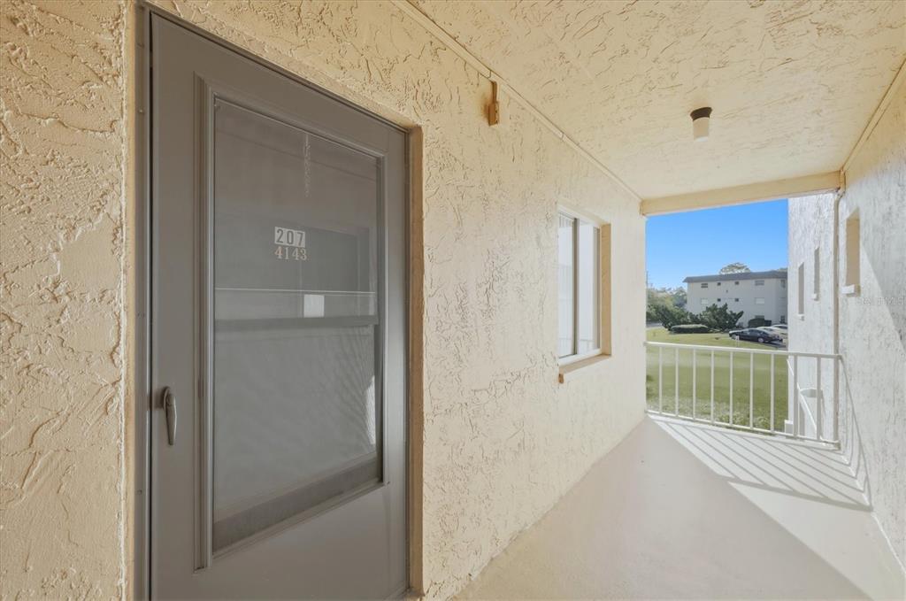 A gray entry door with a screen sits on a covered balcony with textured walls — 4143 HERON WAY 207 BLDG E, BRADENTON, FL