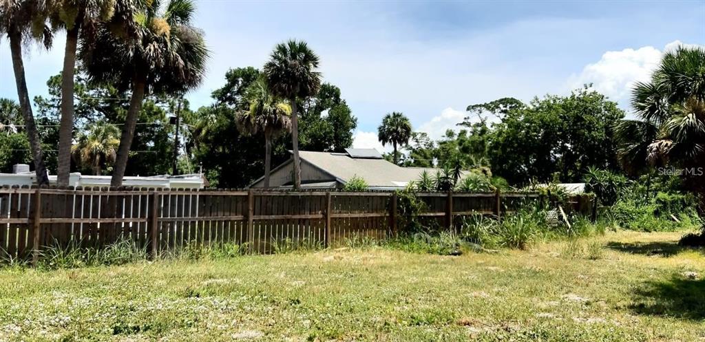 A wooden fence separates a grassy lot from a house surrounded by palm trees — KANAWHA STREET, COCOA, FL