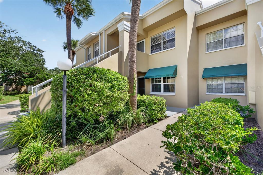 A two-story tan apartment building features green awnings, white railings, and lush landscaping — 10811 INDIAN HILLS COURT UNIT 37, SEMINOLE, FL