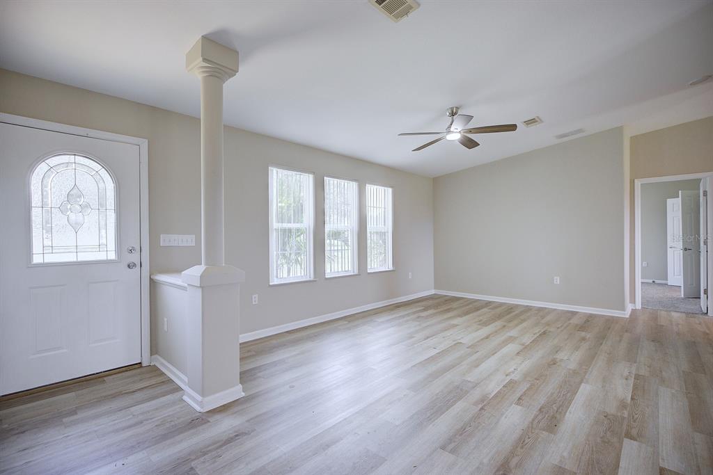 An empty living room features light wood-look flooring, a ceiling fan, and a decorative pillar — 325 STENSTROM ROAD, WAUCHULA, FL